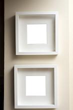 Two empty square neutral colored frames hanging together on an off white wall one below the other