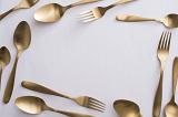 Border of elegant gold cutlery with spoons and forks arranged randomly around central white copy space for food or catering themes