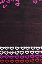 Colorful border of rows of red, white, pink and magenta hearts on dark wood with space for your romantic or love themed message