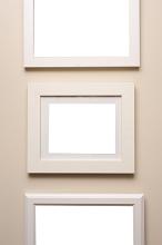 Assorted designs of neutral beige picture frames hanging on a matching colored wall in an art or decor themed background