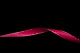 Twisted colorful red ribbon with a shiny metallic border on a black background with copy space for a festive occasion or celebration