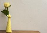 Single yellow rose in giraffe vase border standing in front of a textured neutral off white wall with copy space on a wooden table
