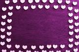 Wooden heart frame arranged in a double row over purple wood conceptual of passion and love with central copy space for your greeting or message to a loved one