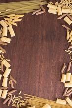 Assorted dried Italian pasta forming a decorative frame over a wooden background with central copy space