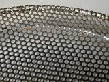 Close up view of shiny metal sheet perforated with many small holes against a gray background