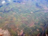 Aerial landscape of agricultural land with fields and pastures under cultivation, farms, a river and town