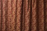 Closed drapes of red and gold brocade curtaining decorated with flowers in a full frame texture background