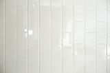 Background texture of long white vertical shiny ceramic tiles with light reflections on a wall, full frame view