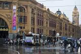 Busy street scene in Melbourne, Australia on a rainy day with passengers and a tram in front of the entrance to the Flinders Street station