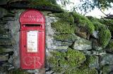 iconic red British post box set into a rural stone wall for the collection of letters and mail for further distribution through the postal services
