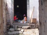 Two Small Children Sitting Together on Door Step of Home with Crumbling Stairs and Stone Walkway on Sunny Day