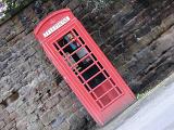 Iconic red British telephone booth on the side of a London street, tilted view against a stone wall