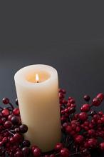 a lit christmas advent candle or table centre with red berries