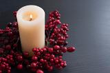 a lit church candle with a wreath of red berries on a plain background