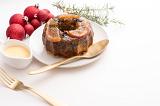 christmas plum pudding with custard or brandy sauce on a plate with cuttlery