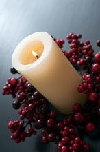 a large chruch candle, lit and surrounded by a wreath of red berries