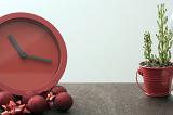 Christmas time concept with festive red clock surrounded by matching decorations on a table with a potted plant and copy space