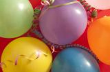Colourful festive background of multicoloured vibrant party balloons with streamers on a red background for a birthday, carnival or festive holiday celebration