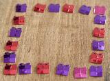 Purple, Pink and Red Foil Confetti Shaped Like Gifts Arranged into Square Border on Wooden Background