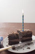 Two remaining slices of a chocolate birthday cake with burning blue candle on a plate with crumbs and knife