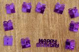 Purple Metallic Birthday Confetti Arranged in Square Border on Wooden Background, Shaped like Wrapped Presents with Birthday Message in Middle