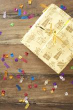 Giftwrapped decorative birthday present with scattered colorful confetti on a wooden table at a birthday party