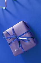 Small Square Gift Box Wrapped in Silver Paper with Shiny Blue Ribbon Tied in Bow on Blue Background