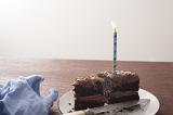 Remnants of a tasty freshly baked chocolate birthday cake with single burning blue candle and knife on a table with napkin and copy space