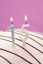 Decorative numeric burning candles for 15th birthday on top of the icing of a glazed birthday cake over a pink background