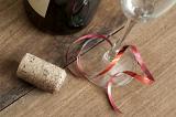 Celebration concept with wineglass tied with a festive red bow and cork on a wooden surface