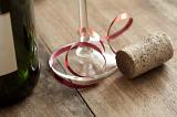 Champagne party background with cork lying on a wooden table beside a bottle and glass decorated with a curled red ribbon