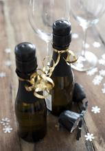 Two Miniature Bottles of Champagne Tied with Gold Ribbon Surrounded by Glasses and Snowflake Confetti for Christmas or New Years Celebration