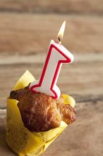 Individual Cake or Muffin Wrapped in Yellow Paper with Burning Candle for First Birthday with Wooden Background