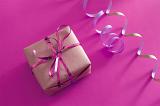 Birthday gift for a girl with a gift wrapped box tied with a pink ribbon and streamer over a pink background, high angle view