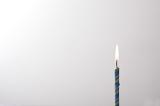 Lone burning blue birthday candle placed to the side over a white background with copy space