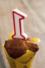 Close Up of Number One Candle Inserted in Muffin or Individual Cake Wrapped in Yellow Paper for First Birthday