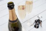 Bottle of luxury champagne with blank gold labeling for celebrating a festive event or holiday, close up high angle view with two full flutes of champagne and a bottle opener behind