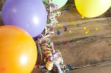 Colorful Inflated Balloons Tied with Curled Ribbon Streamers Surrounded by Birthday Confetti with Copy Space on Wooden Background