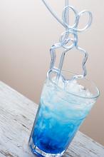 Party ice drink with blue syrup and curved cocktail glass straw in close-up on white wooden table