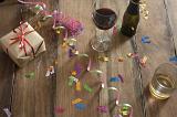 Glasses and Bottle of Wine on Top of Wooden Table with Party Streamers, Confetti and Present in High Angle View.
