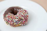 Chocolate doughnut with one half decorated with colorful sprinkles served on a plate for a relaxing coffee break