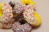 Donut selection with chocolate and orange glazed ring doughnuts dipped in multicolored sprinkles piled on a white background