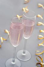 Elegant romantic duo of pink champagne flutes for a party celebration with two twirled gold streamers , high angle on grey