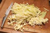 Finely sliced fresh cabbage on a wooden chopping board in the kitchen ready to be used to make a healthy coleslaw salad or to be baked in the oven as a vegetable accompaniment