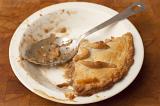 Leftover portion of pie with a golden pastry crust in a plate with a spoon for serving, high angle close up view
