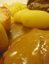 Roast beef dinner with a close up view of a slice of beef covered in rich gravy served with roast potatoes and Yorkshire pudding