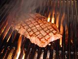 Grilling a tasty tender beef steak on the barbecue over the hot flames on a metal grid at an outdoor summer picnic, close up view