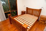 Old fashioned wooden slatted bed frame with no mattress in a room alongside a floor length window on a hardwood floor