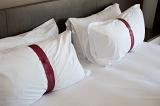 Two white pillows with a decorative band tied around the centre on a double bed, close up background view