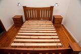 Wooden slatted bed frame with no mattress and two matching bedside tables in a small bedroom